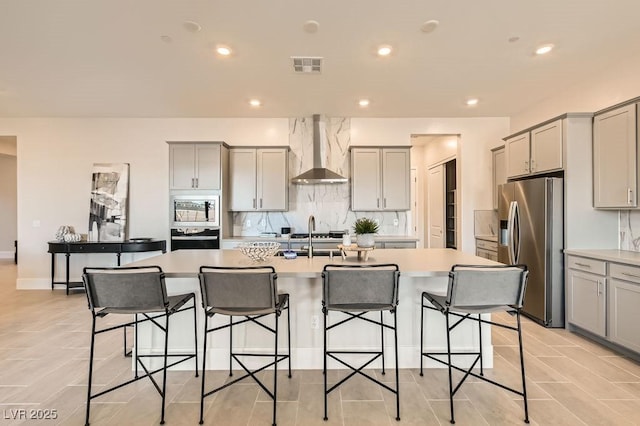 kitchen with a center island with sink, visible vents, wall chimney exhaust hood, appliances with stainless steel finishes, and gray cabinets