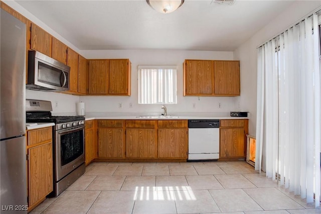 kitchen featuring brown cabinetry, appliances with stainless steel finishes, light countertops, and a sink