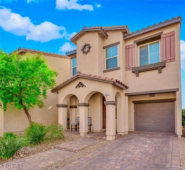 mediterranean / spanish-style house with decorative driveway, an attached garage, a tile roof, and stucco siding