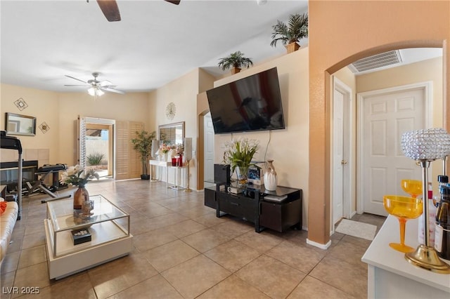 living room featuring light tile patterned floors, visible vents, arched walkways, baseboards, and a ceiling fan