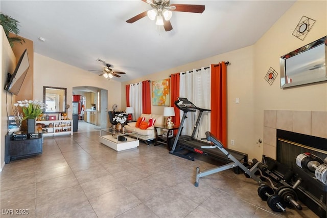 exercise room with arched walkways, ceiling fan, a tiled fireplace, and tile patterned floors