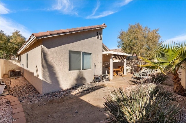 rear view of property featuring a patio, stucco siding, fence, a pergola, and a tiled roof