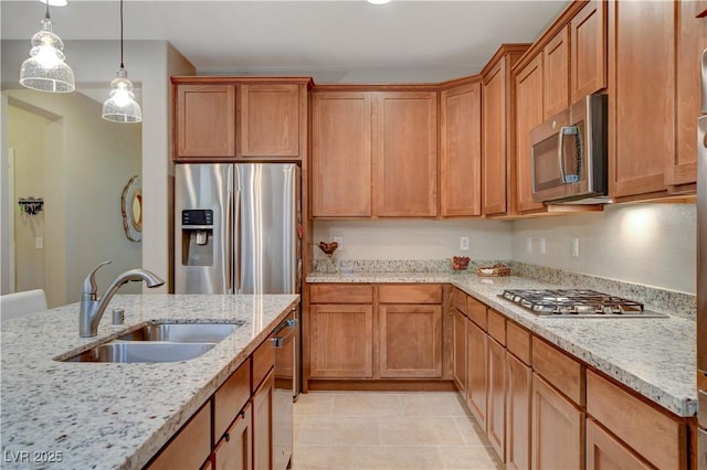 kitchen featuring brown cabinetry, light stone counters, hanging light fixtures, stainless steel appliances, and a sink