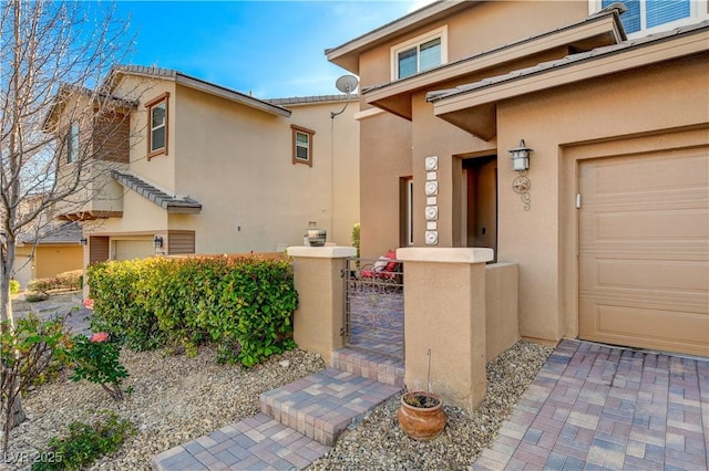 entrance to property featuring a garage, a gate, and stucco siding