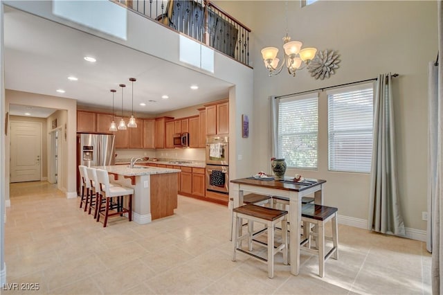 kitchen featuring baseboards, an island with sink, appliances with stainless steel finishes, decorative light fixtures, and an inviting chandelier