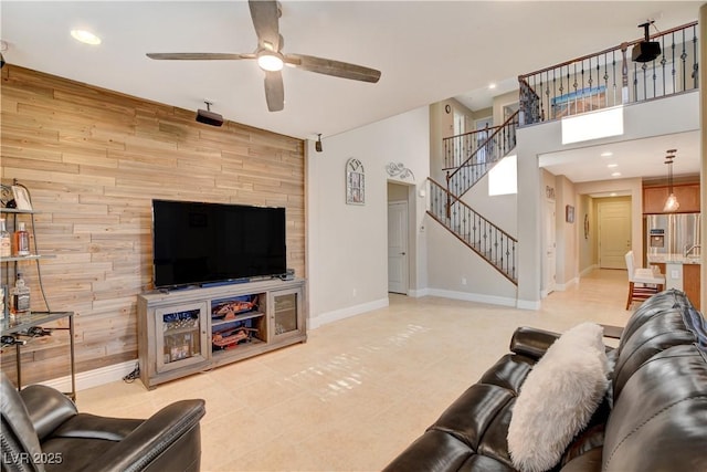 living room featuring a high ceiling, wood walls, baseboards, and stairs