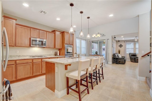 kitchen with a sink, visible vents, hanging light fixtures, appliances with stainless steel finishes, and an island with sink