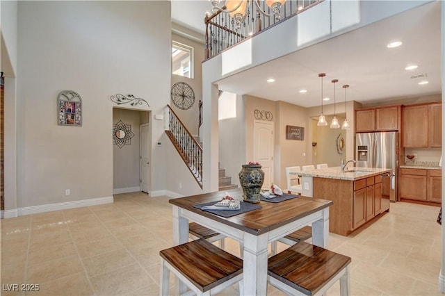 kitchen with a center island with sink, brown cabinets, decorative light fixtures, light stone countertops, and stainless steel refrigerator with ice dispenser