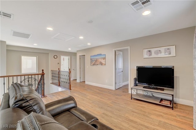 living area featuring baseboards, light wood finished floors, visible vents, and attic access