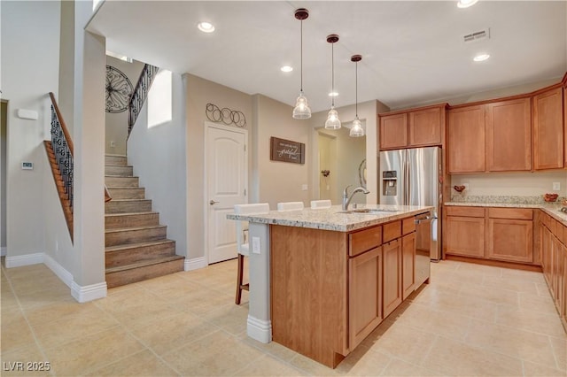 kitchen featuring decorative light fixtures, a center island with sink, visible vents, brown cabinetry, and a sink