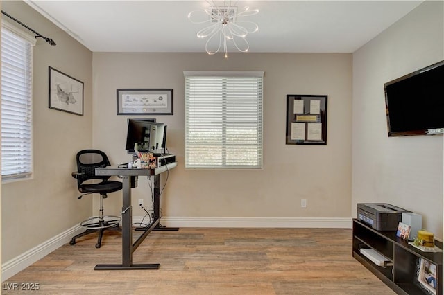 workout room with baseboards, light wood-style floors, and an inviting chandelier