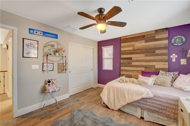 bedroom with visible vents, an accent wall, light wood-style floors, wood walls, and baseboards