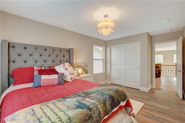 bedroom with a closet, wood finished floors, visible vents, and baseboards