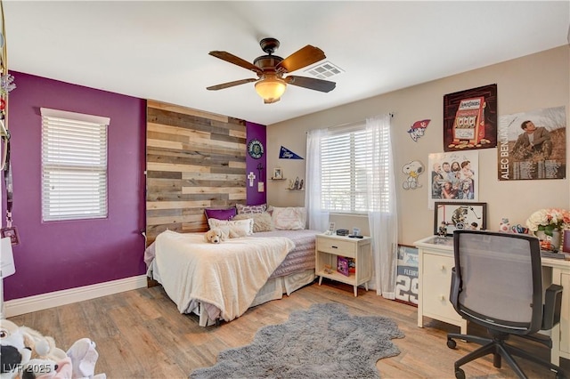 bedroom with an accent wall, wood finished floors, visible vents, and wooden walls