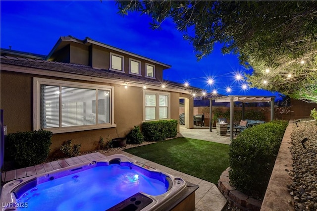 back of house at twilight featuring a pergola, stucco siding, an outdoor hot tub, a patio, and a yard