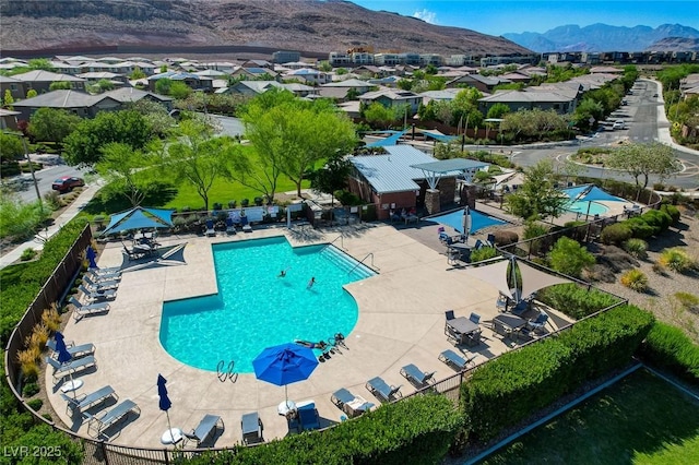 community pool with a residential view, a mountain view, fence, and a patio