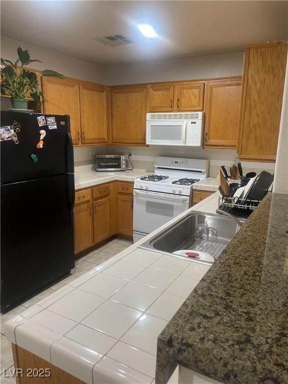 kitchen with white appliances, tile counters, brown cabinetry, and a sink