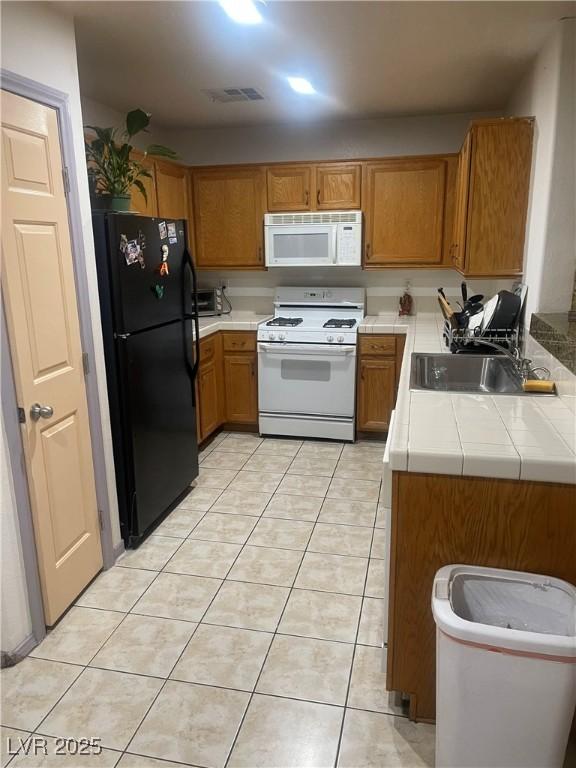 kitchen featuring white appliances, visible vents, brown cabinets, a peninsula, and light tile patterned flooring