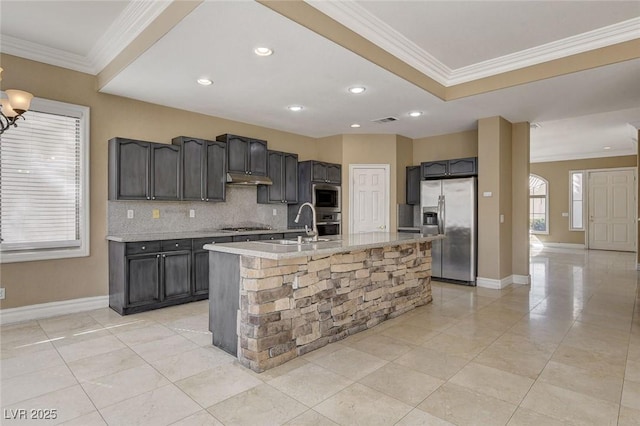 kitchen featuring appliances with stainless steel finishes, crown molding, under cabinet range hood, and an island with sink