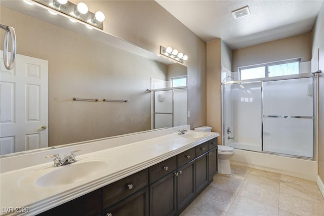 bathroom featuring toilet, shower / bath combination with glass door, a sink, and visible vents