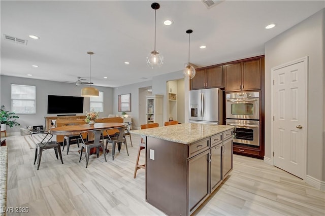 kitchen featuring light stone counters, open floor plan, a center island, hanging light fixtures, and stainless steel appliances