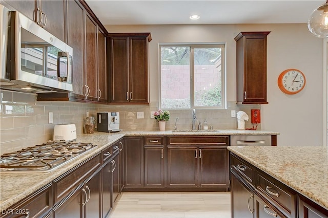 kitchen with dark brown cabinetry, appliances with stainless steel finishes, light stone counters, a sink, and backsplash