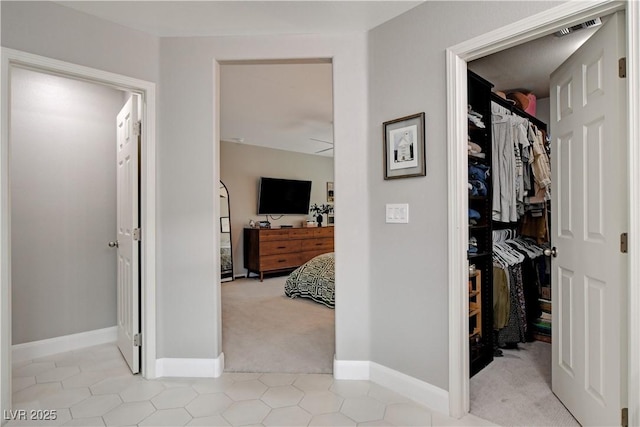 hall with light carpet, visible vents, and baseboards