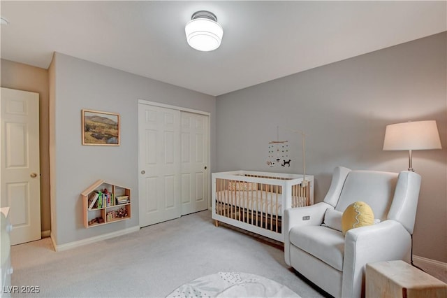 bedroom featuring baseboards, a crib, a closet, and light colored carpet