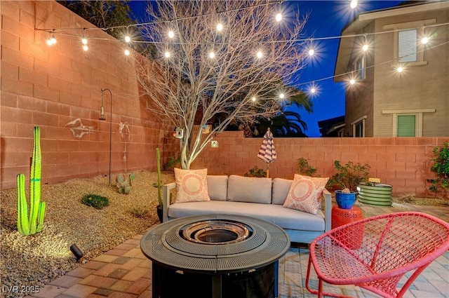 patio at night with an outdoor living space with a fire pit and a fenced backyard