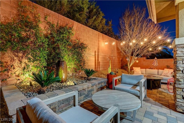 patio at night featuring an outdoor living space with a fire pit and a fenced backyard