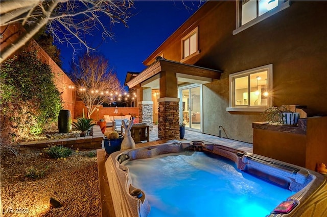 pool at night featuring hot tub deck surround and a fenced backyard