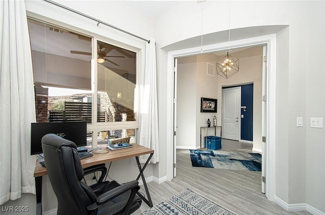 home office with ceiling fan with notable chandelier, visible vents, baseboards, and wood finished floors