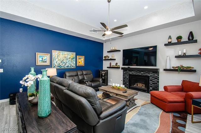 living area featuring recessed lighting, a glass covered fireplace, wood finished floors, baseboards, and a raised ceiling