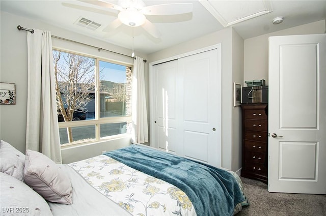 carpeted bedroom with a closet, attic access, visible vents, and a ceiling fan