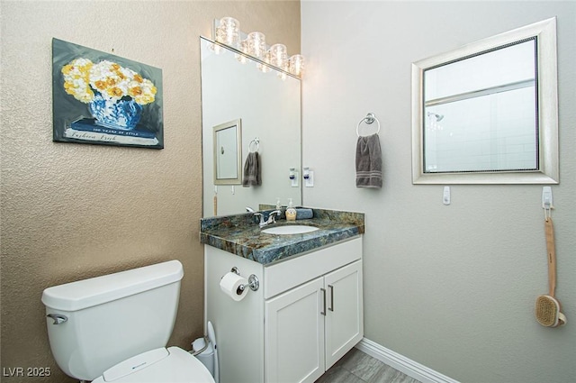 bathroom with a textured wall, vanity, toilet, and baseboards