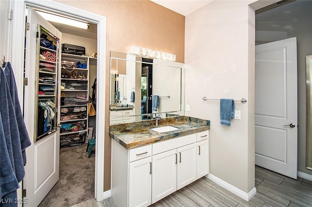 full bathroom with wood tiled floor, vanity, baseboards, and a spacious closet