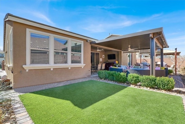 back of property featuring a patio area, a yard, a ceiling fan, and stucco siding