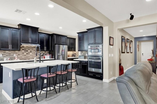 kitchen featuring visible vents, appliances with stainless steel finishes, open floor plan, dark cabinets, and a kitchen bar