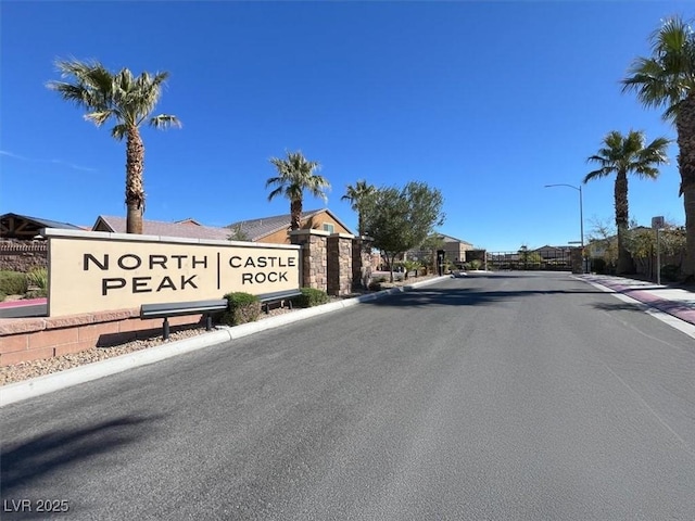 view of road featuring sidewalks, curbs, a gated entry, and street lights