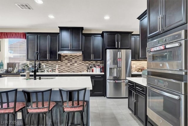 kitchen with appliances with stainless steel finishes, light countertops, visible vents, and dark cabinetry