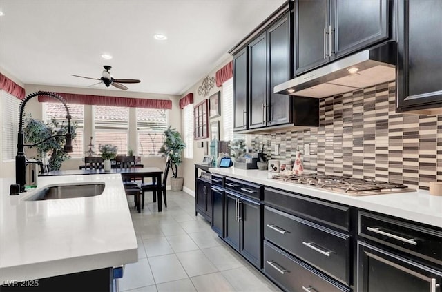 kitchen with stainless steel gas cooktop, light tile patterned floors, light countertops, a sink, and under cabinet range hood