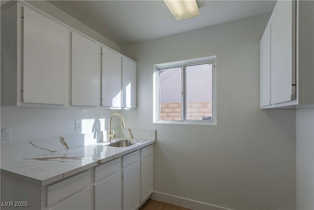 kitchen with baseboards, a sink, light stone countertops, and white cabinets