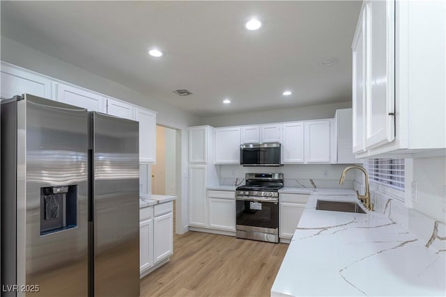 kitchen featuring light stone counters, stainless steel appliances, visible vents, white cabinets, and a sink