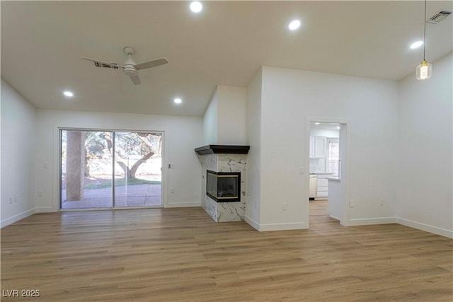 unfurnished living room with light wood-type flooring, ceiling fan, a premium fireplace, and visible vents