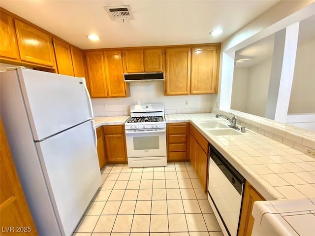 kitchen featuring white appliances, brown cabinetry, visible vents, and under cabinet range hood