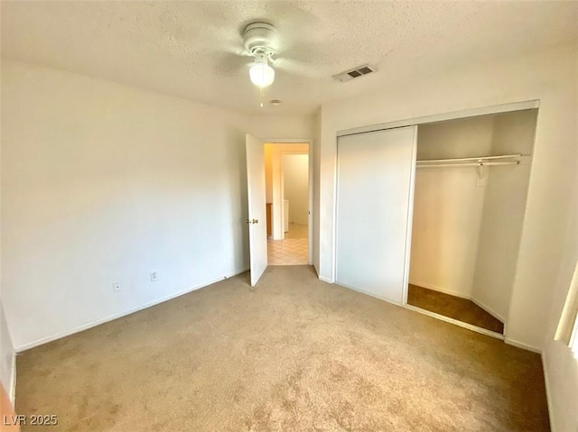 unfurnished bedroom with a textured ceiling, light carpet, visible vents, a ceiling fan, and a closet