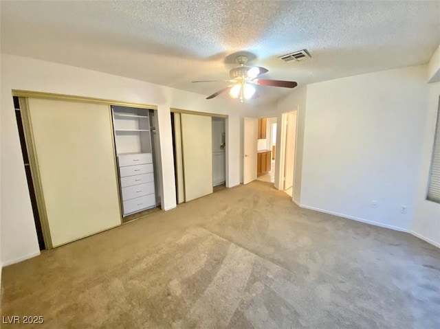 unfurnished bedroom with visible vents, light colored carpet, ceiling fan, a textured ceiling, and multiple closets