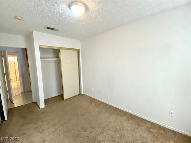 unfurnished bedroom featuring carpet, a textured ceiling, visible vents, and a closet