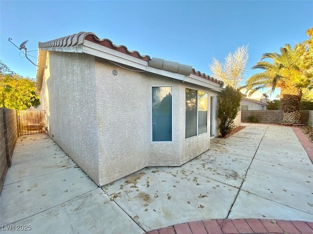 view of property exterior featuring fence private yard, a patio area, a tiled roof, and stucco siding