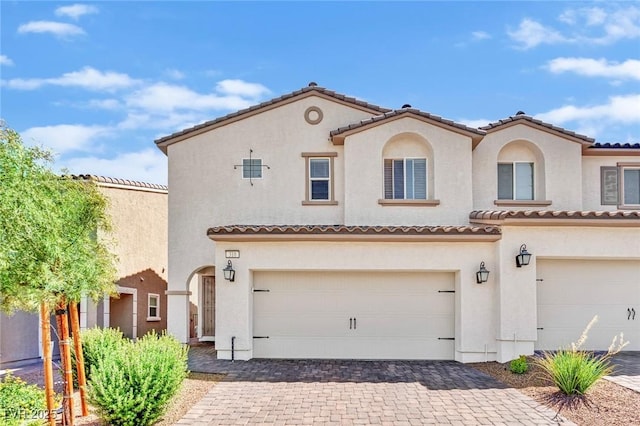 mediterranean / spanish-style home featuring decorative driveway, a tiled roof, an attached garage, and stucco siding